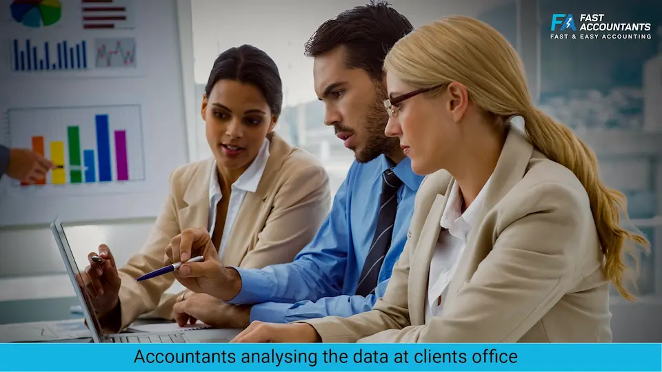Three business professionals—two women and one man—sitting at a desk in a modern office, analyzing data on a laptop. A chart board with colorful graphs is visible in the background, indicating a client meeting or financial discussion. The group appears focused and collaborative.